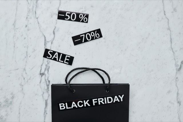 Schaufenster mit großen roten Black-Friday-Sale-Schildern und Menschen mit Einkaufstüten